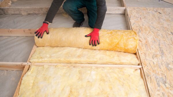 A technician in gloves rolls out yellow insulation batts into flooring.