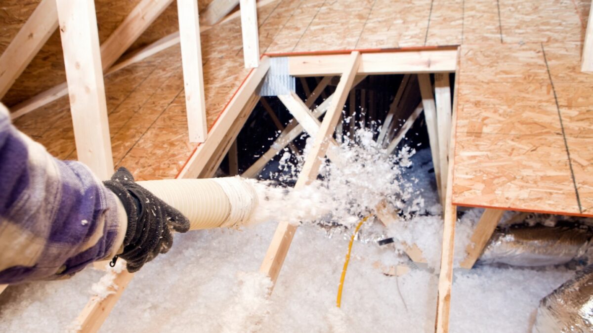 A technician uses a hose to install blow-in insulation.