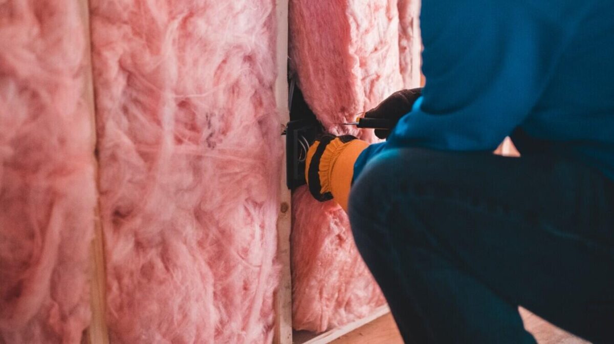Insulation installation expert kneels to install pink insulation into a wall