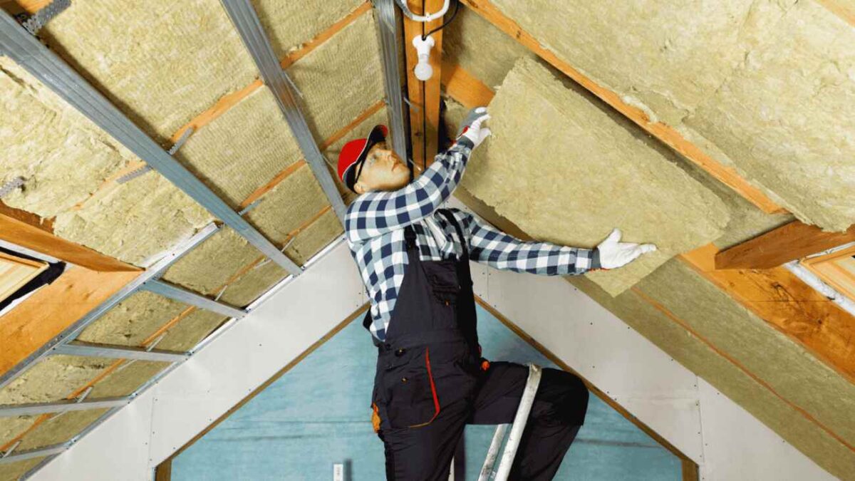 Man stands on a ladder installing insulation